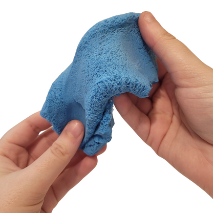 A person's hands stretch and play with blue Sticky Sand.