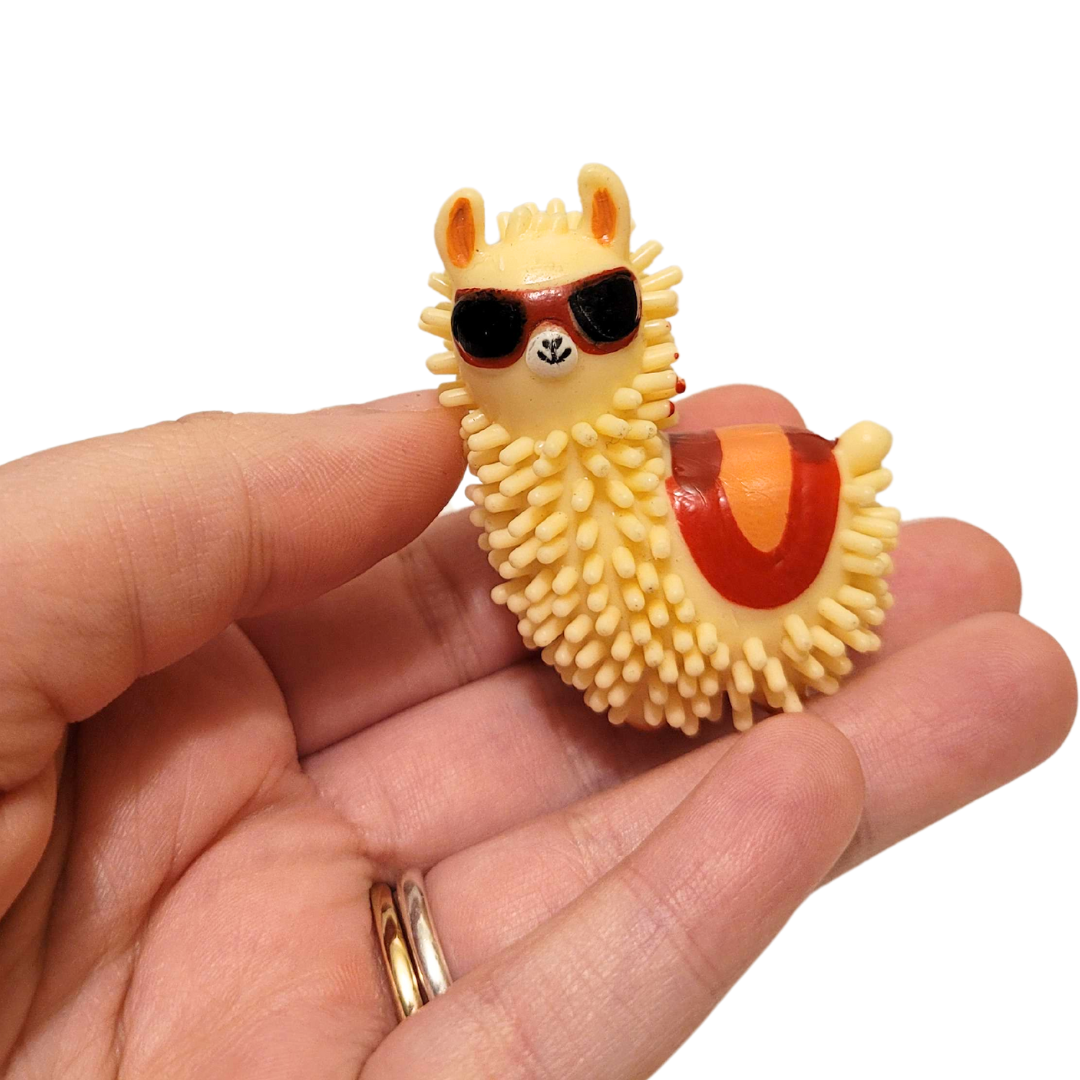 A person's hand holds out a spiky llama in sunglasses figure with brown and orange accents.