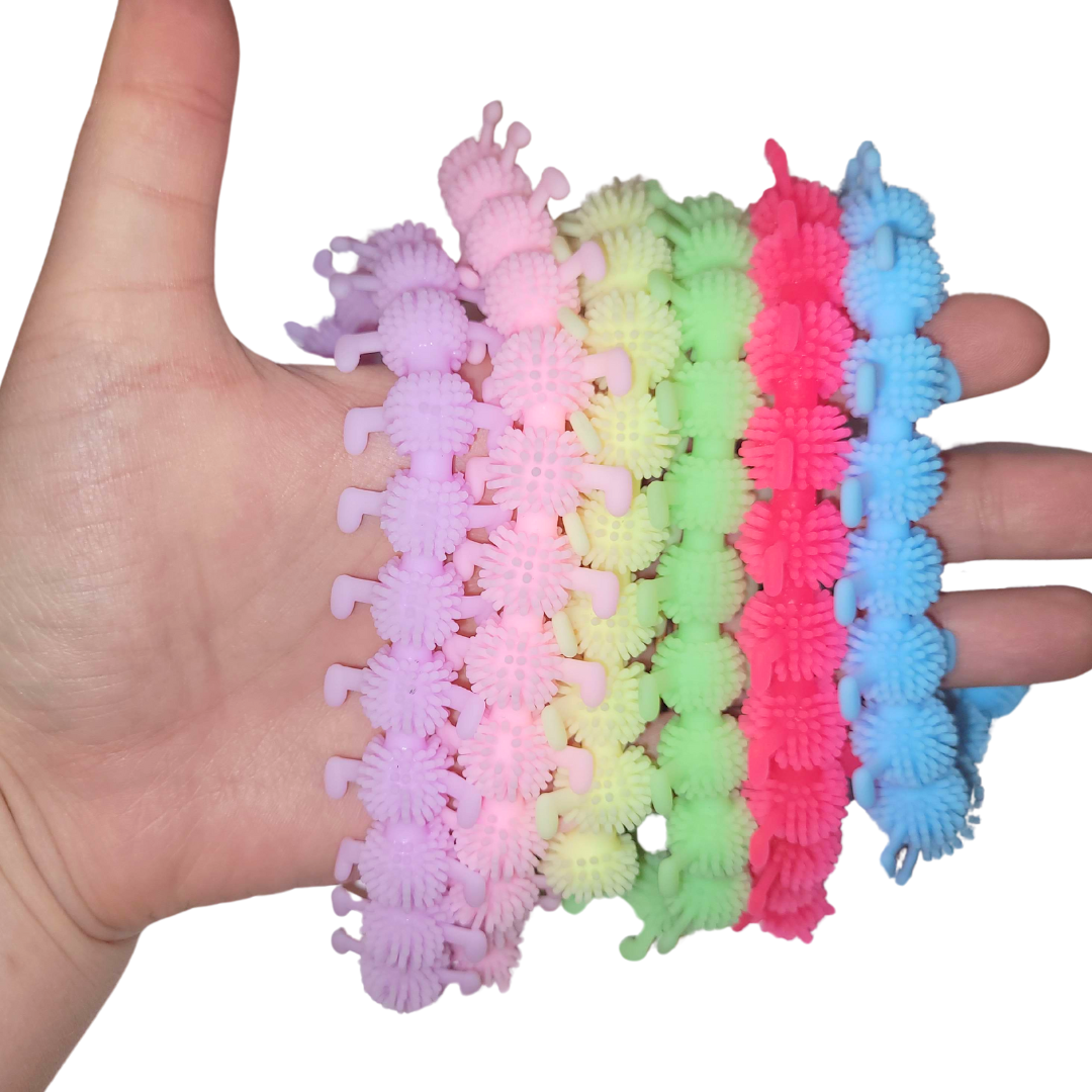 A person's hand holds out six stretchy caterpillars in different colors. The colors are, from left to right, lavender, light pink, pastel yellow, lime green, hot pink, and light blue.