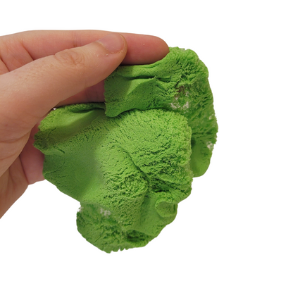 A person's hand holds out a clump of green Sticky Sand.