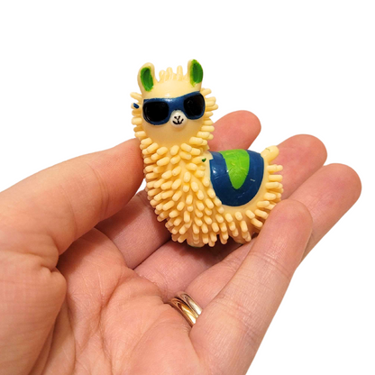 A person's hand holds out a spiky llama in sunglasses figure with blue and green accents.
