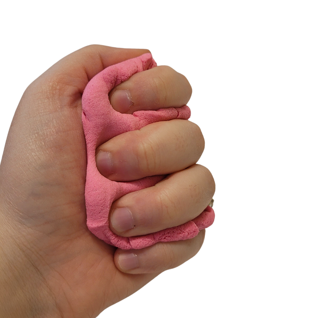 A person's hand squeezes pink Sticky Sand.