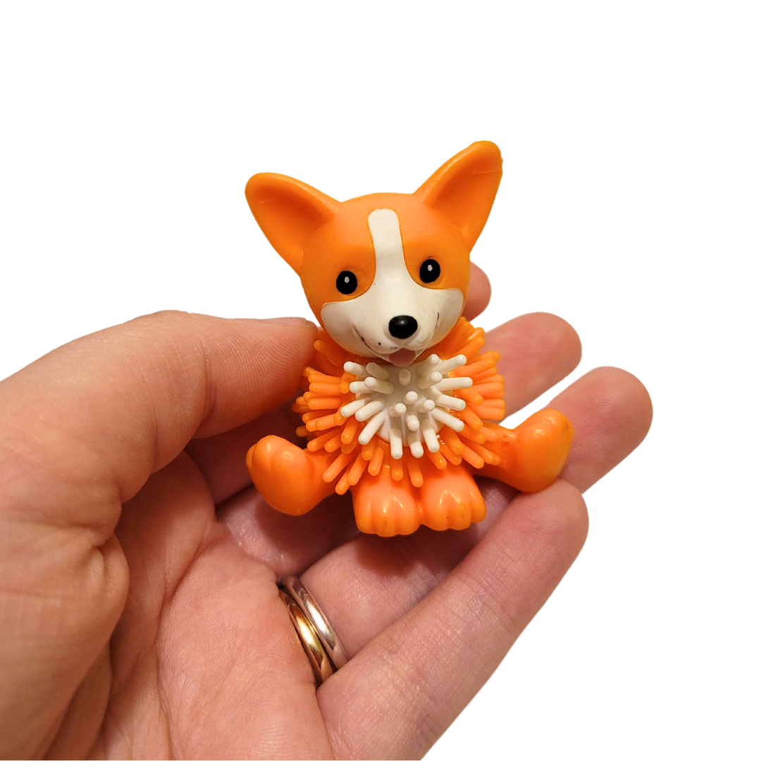 A person's hand holds out an orange spiky corgi figure.