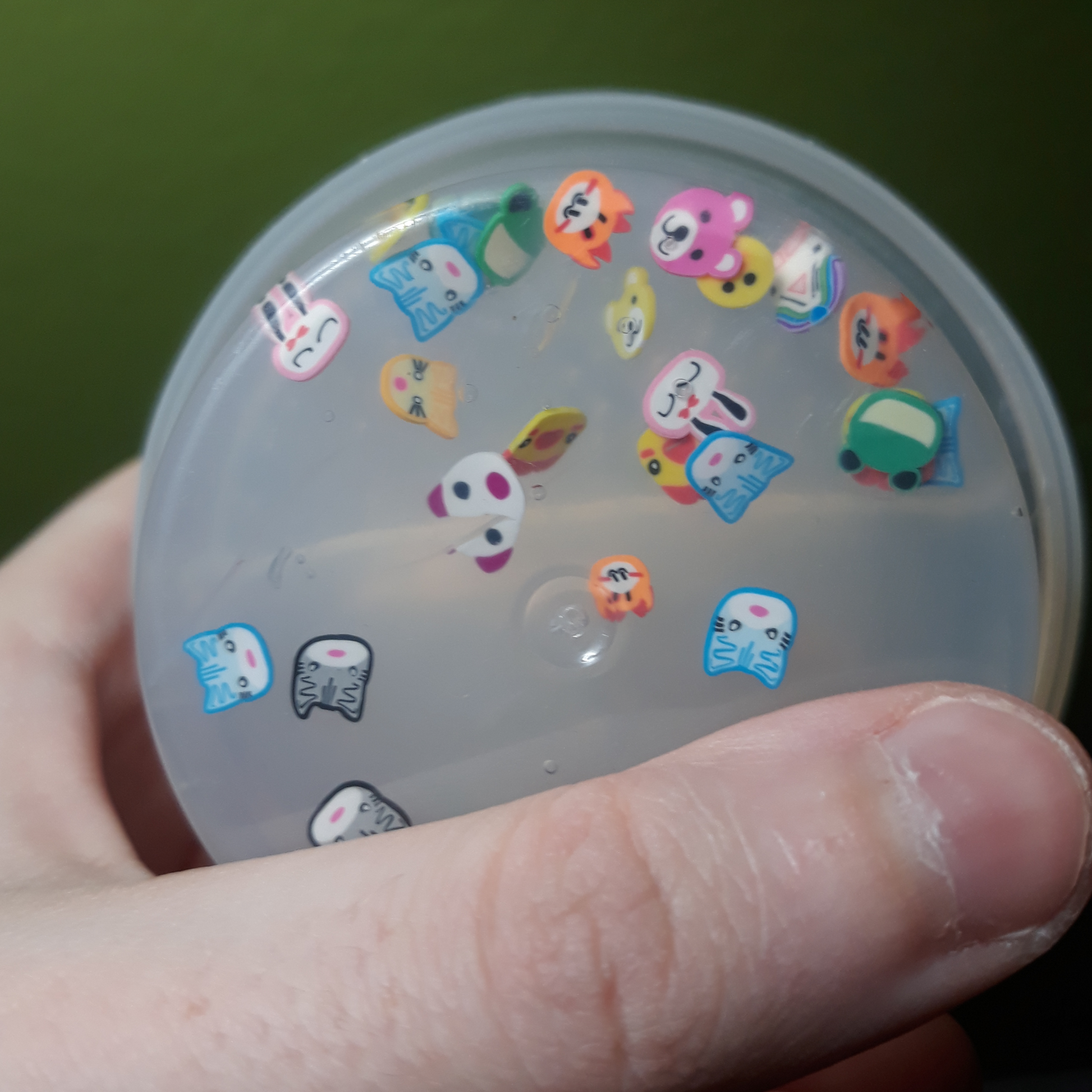 A hand holding a container of clear slime with animal friends, and showing the animals contained up close.